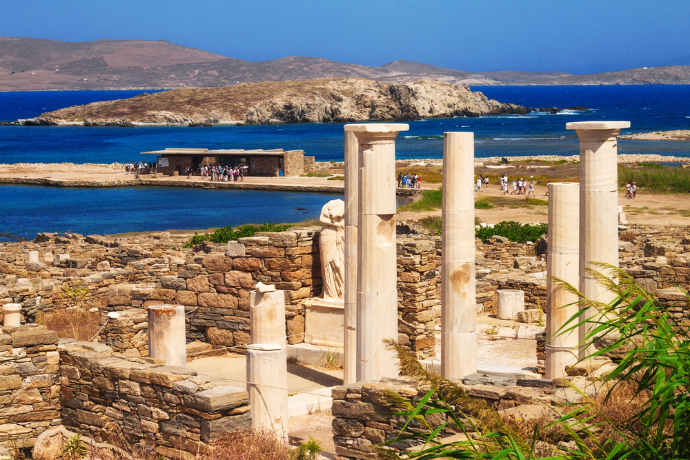Ancient marble ruins on Delos Island with columns and statues under a blue sky, near Mykonos, Greece