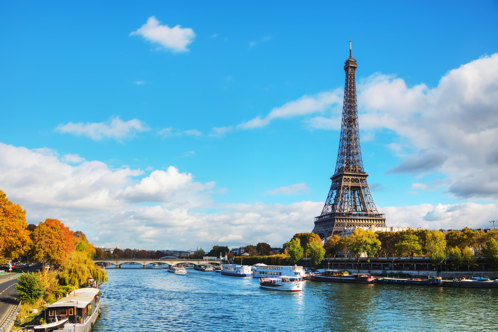 Sightseeing cruise boat passing under a bridge on the Seine River with views of Notre-Dame and historic buildings in Paris, France