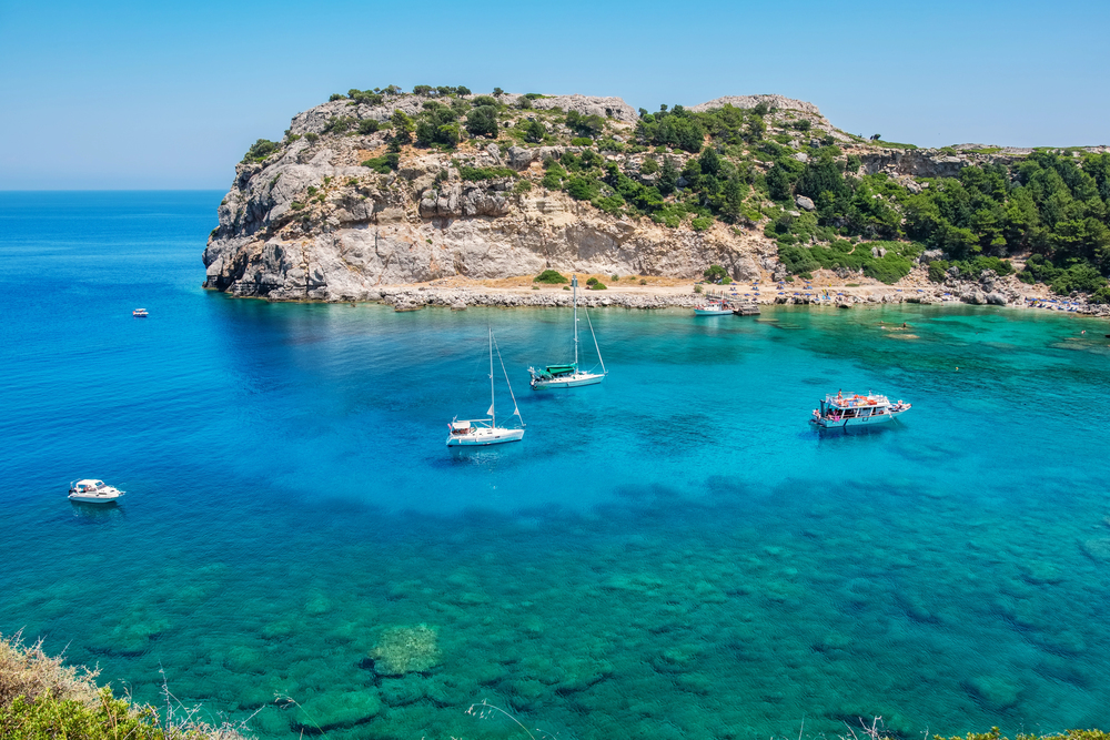 Boat anchored in turquoise waters off the coast of Rhodes with people swimming and relaxing in the sun