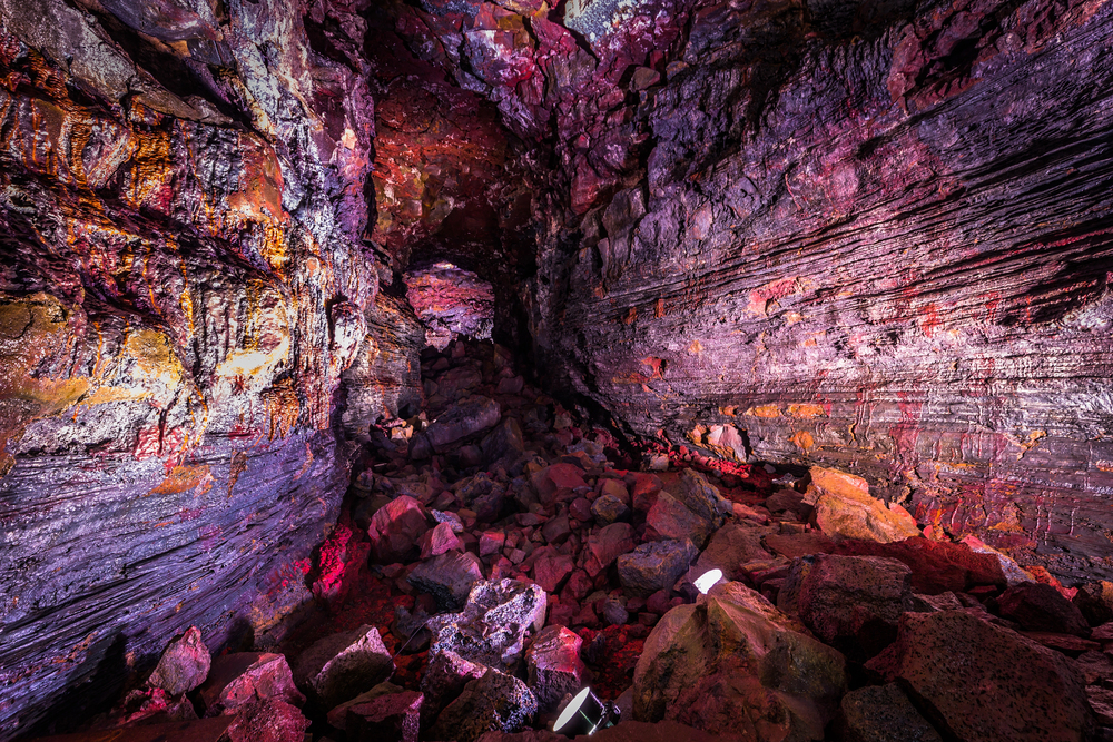 Inside the Raufarhólshellir lava tunnel in Iceland with dramatic rock formations and natural light beams shining through the cave roof