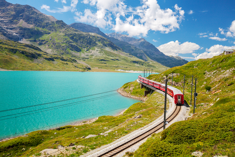 The red Bernina Express train crossing a stone viaduct in the Swiss Alps with snow-covered peaks near St. Moritz