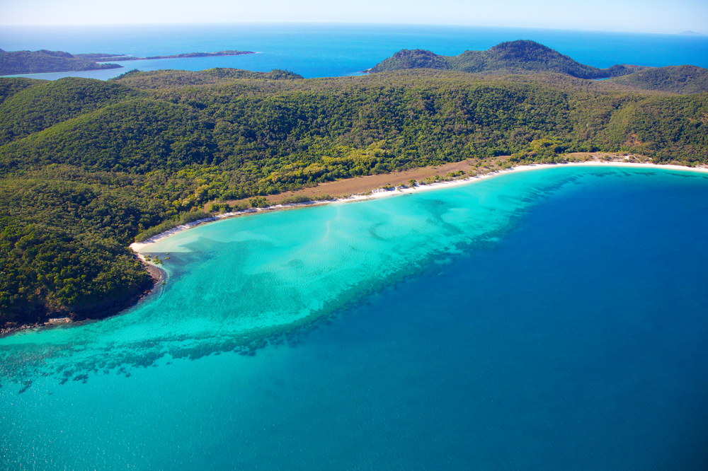 Snorkelers in clear turquoise water at the Great Barrier Reef with a catamaran and helicopter flying overhead near Cairns, Australia