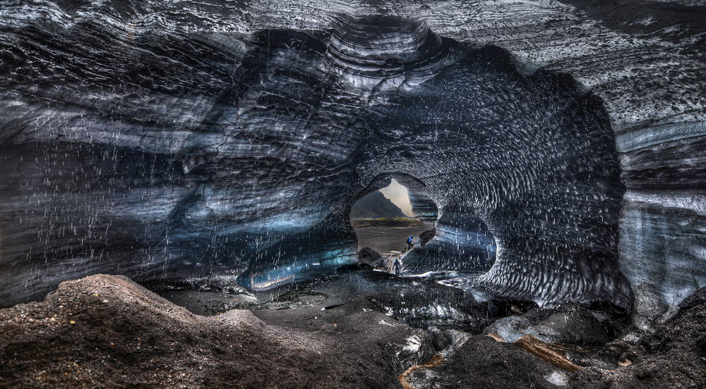 Inside the Katla Ice Cave near Vík with streaks of black volcanic ash and glistening blue ice walls in Iceland