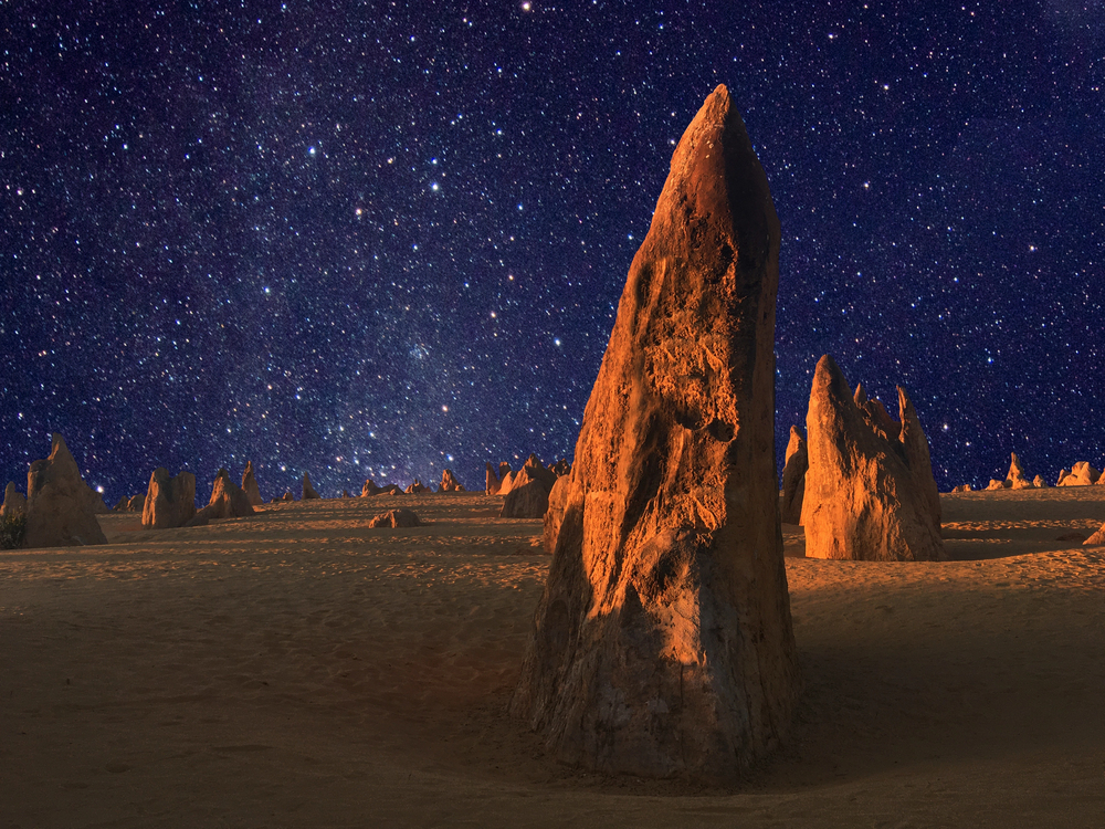 Limestone rock formations glowing under a golden sunset in the Pinnacles Desert with stars visible in the twilight sky, Western Australia