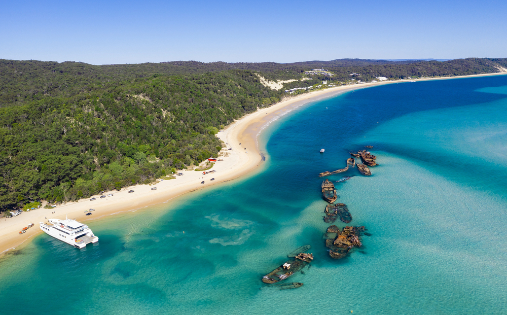 Snorkelers exploring the Tangalooma Wrecks in clear blue water off Moreton Island with sandy beaches in the background, Queensland, Australia