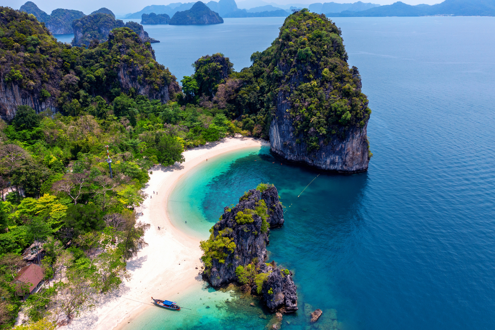 Longtail boat floating in the crystal-clear lagoon of Hong Island surrounded by limestone cliffs in Krabi, Thailand