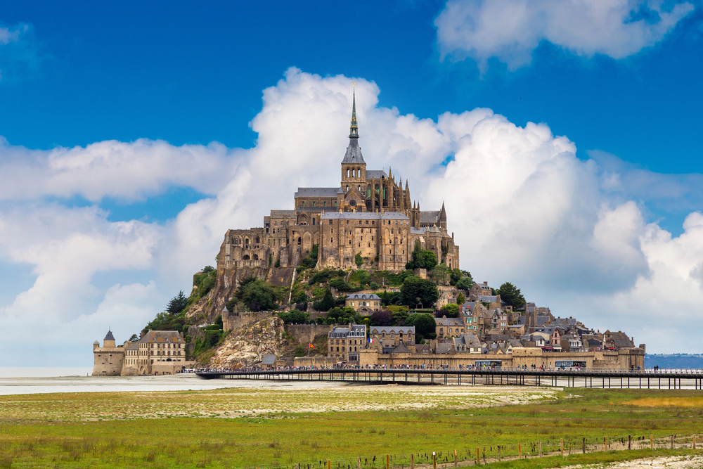 Mont Saint-Michel island rising from the tidal bay with abbey at the top under a blue sky, Normandy, France