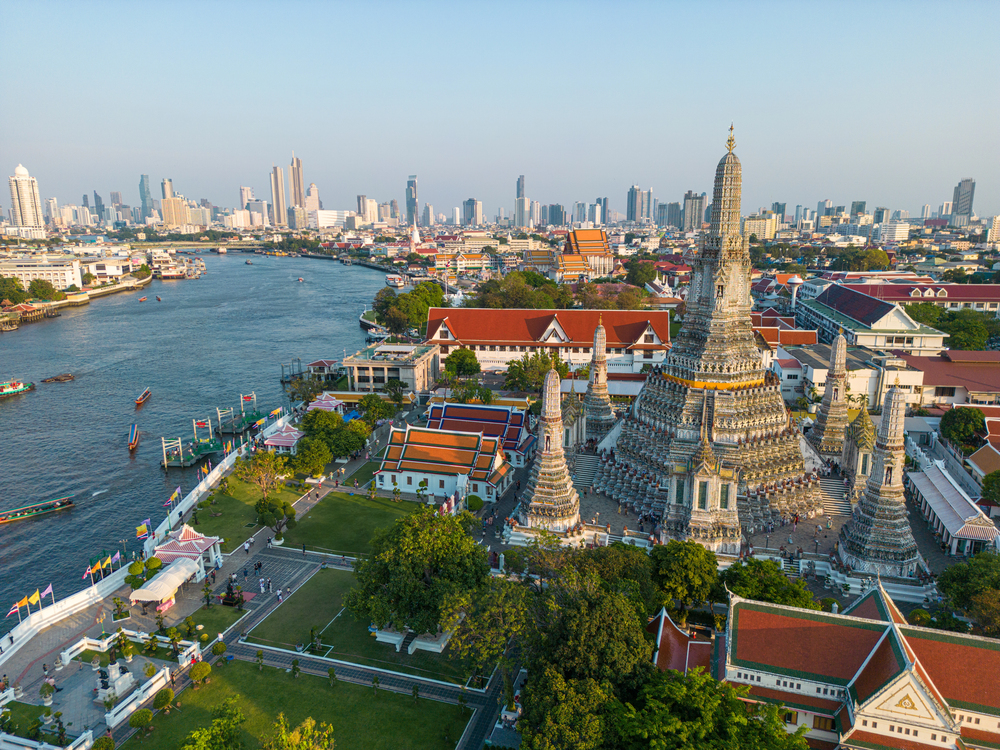Wat Arun temple spires along the Chao Phraya River with golden sunlight in Bangkok, Thailand