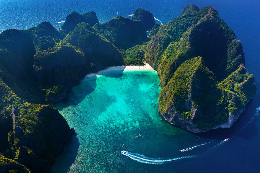 Longtail boats floating in clear turquoise water with limestone cliffs in the background at Maya Bay, Phi Phi Islands, Thailand