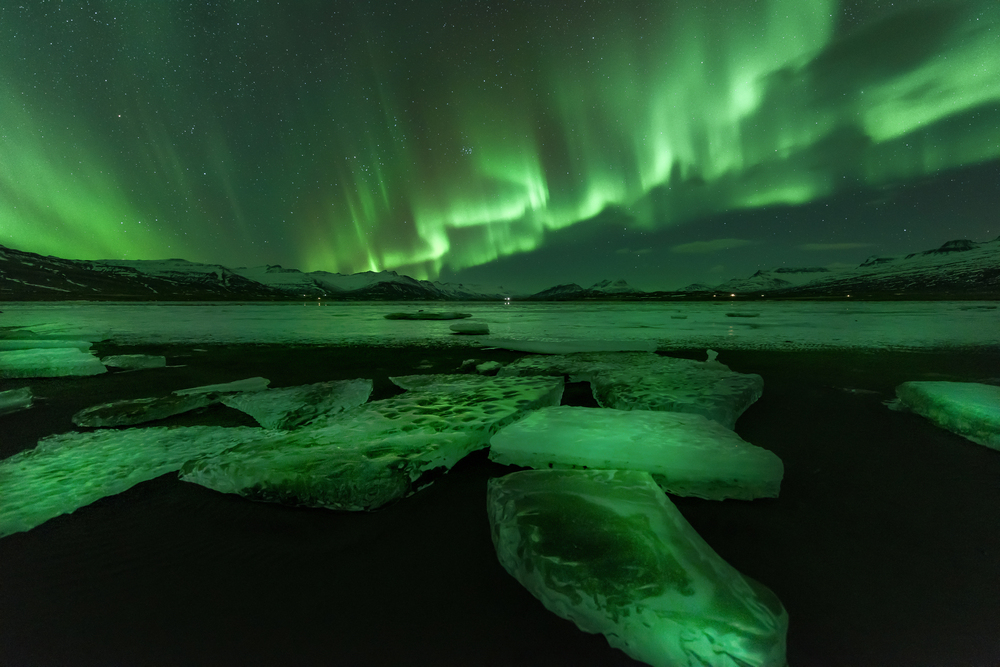 Northern Lights glowing in green and purple over snowy fields outside Reykjavik on a night tour in Iceland