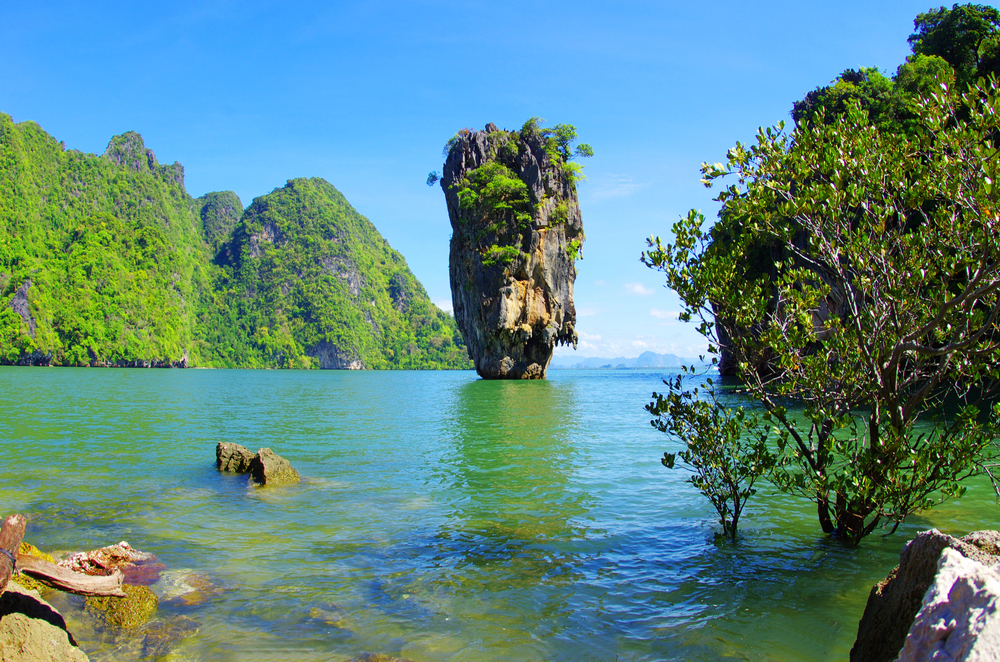 Longtail boat cruising past limestone karsts and calm water in Phang Nga Bay National Park, Thailand
