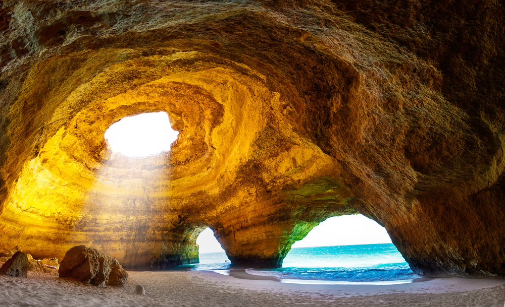 Boat entering the Benagil Cave along Portugal’s Algarve coast, with sunbeams shining through the skylight and turquoise water below.